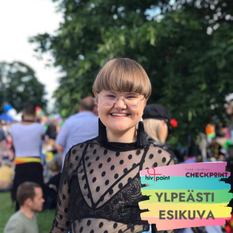 Havu hymyilee iloisesti Pride-puistojuhlassa täplikkäässä paidassa. Kuvan alalaidassa on sateenkaarilippu, jossa lukee: ylpeästi esikuva