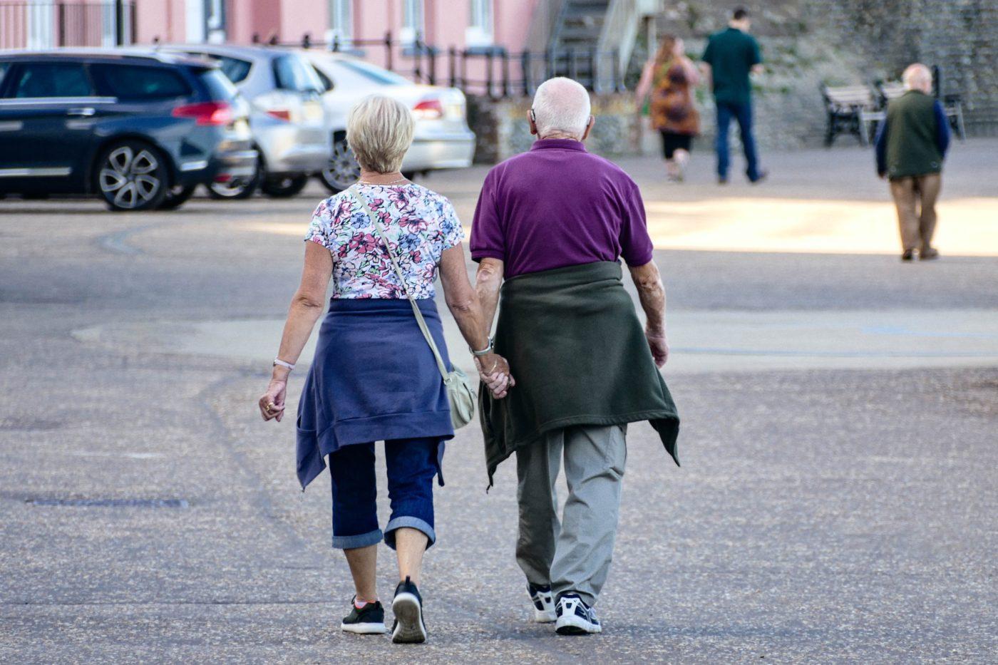 Ageing with HIV. In the photo two gray haired persons are walking on the street hand in hand.