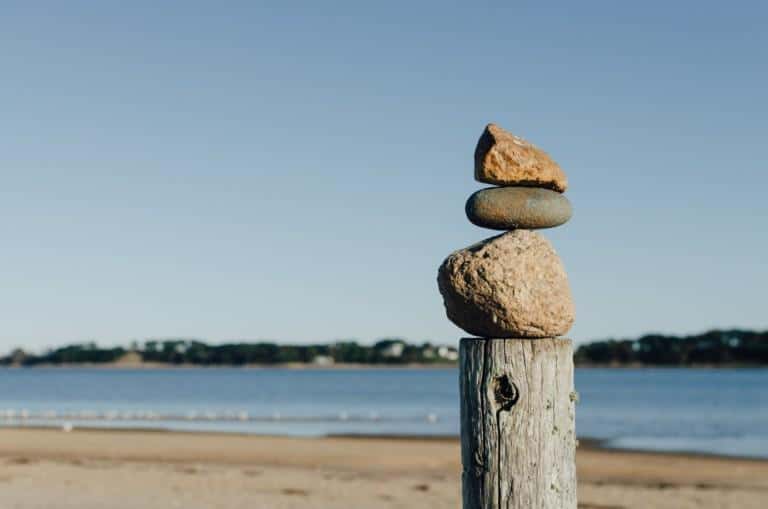 In the foreground of the picture is a wooden log on which stones are placed on top of each other. An oceanview.