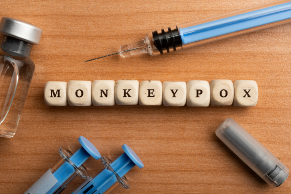 Kirjainkuutioista muodostunut sana monkeypox, lääkepullo, ruiskuja, neula