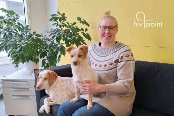 Sohvalla istuu Hivpointin hankekoordinaattori Niina Laaksonen iloisesti hymyillen koiriensa Sidin ja Jäggerin kanssa.