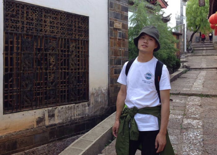 Hivpoint's Health Buddy Hong is standing in an alley with Asian style decorations.