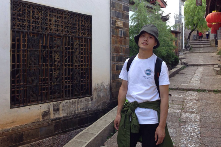 Hivpoint's Health Buddy Hong is standing in an alley with Asian style decorations.