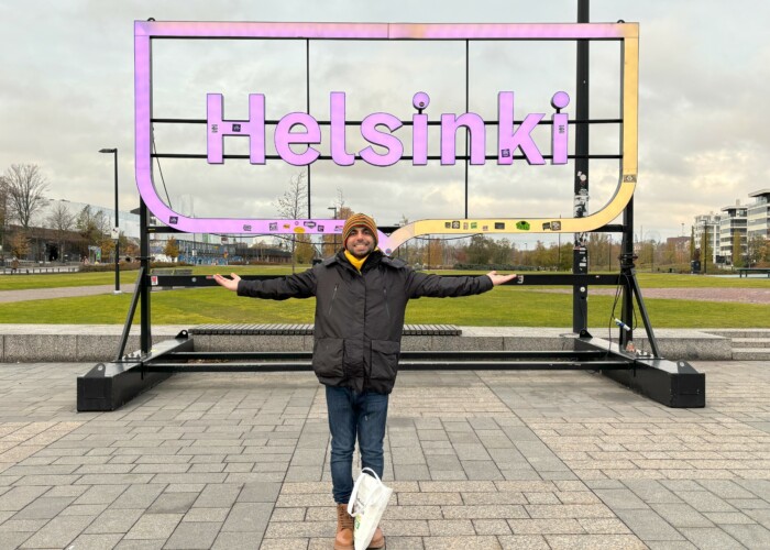 Health Buddy Ali is standing outside in front of the Helsinki sign.