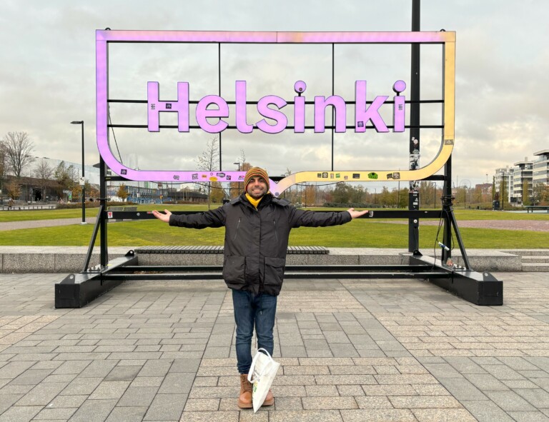 Health Buddy Ali is standing outside in front of the Helsinki sign.