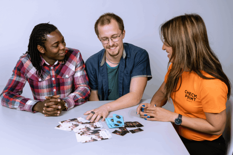 Three people are talking to each other, smiling. In front of them, there are brochures and condoms on the table.