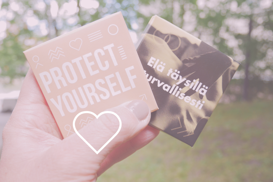 Sormet pitävät kädessä kahta turvaseksipakkausta, joissa toisessa lukee "Protect Yourself" ja toisessa "Elä täysillä turvallisesti"