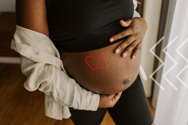 A pregnant person is holding their belly. There is a heart symbol on the belly.